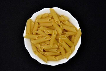 Wheat pasta in a white bowl on a black background. Dry pasta.