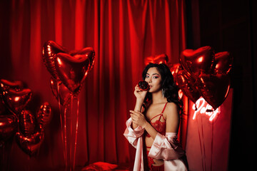 Portrait of smile sexy asian girl glam makeup in lingerie with cupcake among red shiny balloons