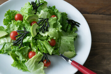 White plate of mixed salad with seaweed, tomatoes, lettuce and avocado. Wood background. Copy space.