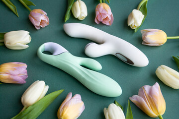 Two toys for adults lie on a green background, surrounded by tulips - 580803259