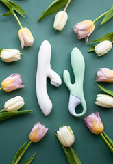 Two toys for adults lie on a green background, surrounded by tulips - 580803262