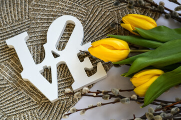 A bouquet of yellow flowers and wooden white letters lie on the table. Tulips spring flowers. Love and romance concept.