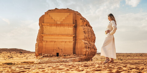 Young Caucasian woman in long white dress posing in front Tomb Lihyan Son of Kuza or Qasr al-Farid...