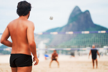 rear view of brazilian man in swimsuit playing footvolley or futevolei in lpanema, Brazil
