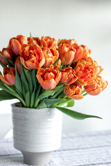 Bouquet of orange tulips in a vase on a blurred light background.