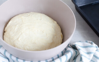 A bowl with dough and a cooking spatula on the table. The process of making Pampushky, traditional Ukrainian buns for borsch. The concept of traditional dishes. Homemade baking. Horizontal orientation