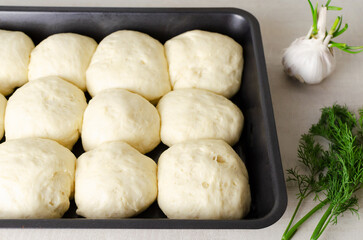 Future buns in baking form with garlic and dill on the table. Preparation of pampushky (Pampushky), traditional Ukrainian buns for borsch. Concept of Homemade baking. Horizontal orientation.