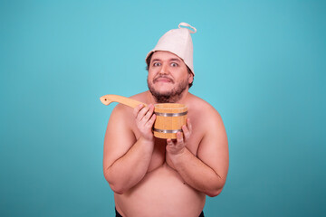 Funny fat man in a hat and with a sauna ladle. Blue background. Taking a shower.