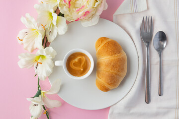 Top view of croissant on a white plate with a cup of espresso coffee with a heart on it, flowers...