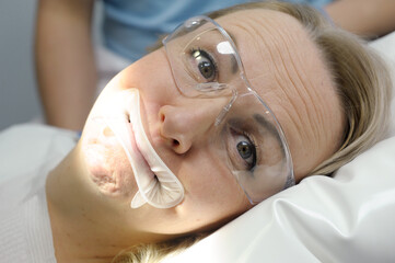 woman in dental chair optragate mouthpiece holding lips for dental procedures in transparent glasses opens and closes mouth grimaces making faces smiling cheerful dentistry funny close-up