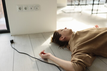 Woman lies on the floor with her eyes closed near electric cable with plug.