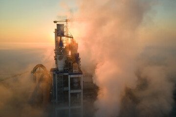 Aerial view of cement factory with high concrete plant structure and tower crane at industrial manufacturing site on foggy evening. Production and global industry concept