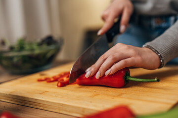 Close up view of woman’s hand cutting a red pepper with a kitchen knife