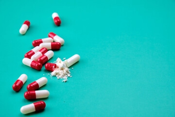 Several capsules, some of them open, spilling a white powder on a green table.