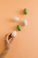 Fototapeta na wymiar Easter pattern made of white and green eggs and woman's hand on pastel orange background. Minimal Easter holiday composition. Creative food concept. Top view, flat lay.