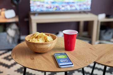 Close up of smartphone with sports bets app on screen against football match in home setting, copy space