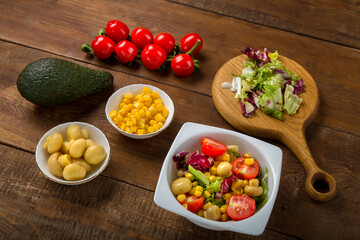 Vegetable salad with lettuce and cherry tomato with avocado olive oil in a white plate on a wooden table next to all the ingredients.