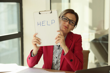 Manager woman showing paper with word help while sitting at her desk.
