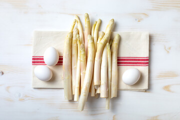Bunch of raw white asparagus with eggs on white wooden table. Top view, copy space