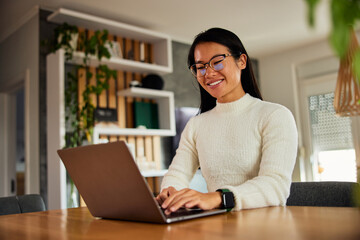 A smiling Asian businesswoman typing on a laptop, sitting in the living room.