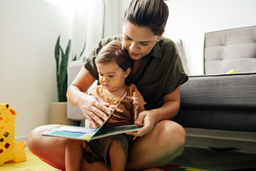 Mom reading a book with baby boy at home. Early age children education, development. Mother and...