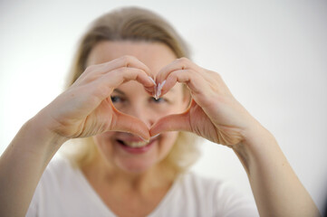woman shows her heart with her hands a cheerful look through her hands at the camera white background interest fun joy pleasant emotions happiness