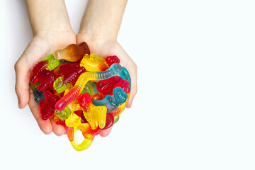 A large pile of multi-colored jelly marmalade candies in the hands of a child on a white...