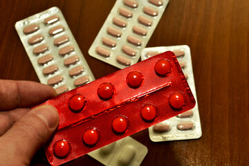 In a man's hand, a red blister with ten medical pills close-up, against the background of other medicines