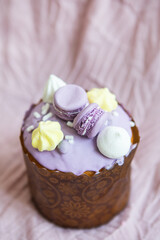 A traditional paska decorated with white Swiss chocolate and meringue stands on a lavender tablecloth. Easter holiday.