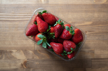 Ripe red strawberries in plastic box on wooden table