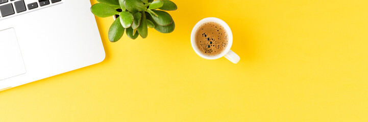 Office desktop with laptop, coffee and small succulent on yellow background with copyspace