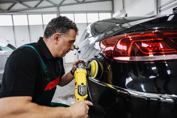 Professional car service worker polishing luxury car with orbital polisher in a car detailing and...