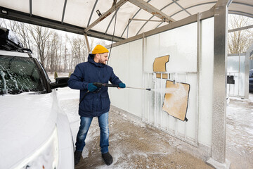 Man washing high pressure water car carpets at self service wash in cold weather.