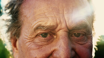 One senior person close up face and eyes with sunlight flare. Wrinkled elder mature 70s male person outside