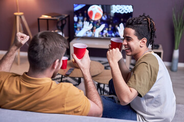 Fototapeta premium Group of excited sports fans watching basketball match on TV at home and drinking beer