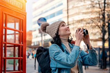 Outdoor portrait of woman using camera   against red phonebox in English city - obrazy, fototapety, plakaty