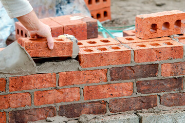 Hard working bricklayer lays bricks on cement mix on construction site. Fight housing crisis by building more affordable houses concept - obrazy, fototapety, plakaty
