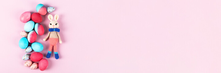 Painted Easter eggs in crimson and blue with crocheted easter bunny on a pink background with a...