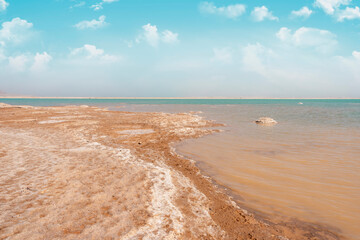 sandy salty beach of the Dead Sea and cloudy blue sky in Israel in sunny hot day