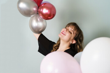 Young Woman Posing and Holding Balloons in Hand Against Grey Background