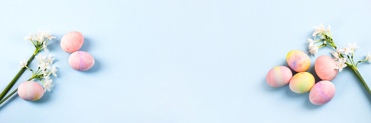 Spring white flowers daffodils and pink Easter eggs on a blue background with space for text. Happy Easter concept. Greeting card, copy space, banner