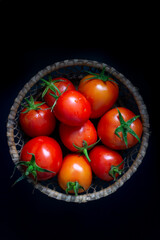top view of fresh tomatoes inside a wicker basket arranged on a black background in a dark room with studio lighting
