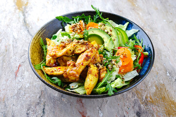 Traditional German iceberg and Italian arugula salad served with chicken, avocado and vegetables with spicy sweet and sour curry sauce as close-up on a rustic plate with text space