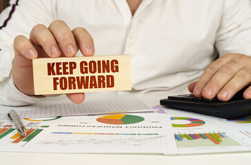 On the table are business charts and diagrams in the hands of a wooden block with the inscription - Keep Going Forward