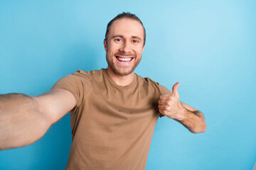 Photo of pretty confident man wear beige t-shirt showing thumb up tacking selfie isolated blue...
