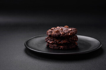 Delicious fresh oatmeal round cookies with chocolate on a black ceramic plate