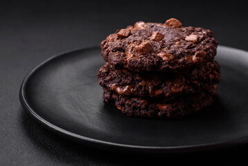 Delicious fresh oatmeal round cookies with chocolate on a black ceramic plate