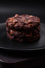 Delicious fresh oatmeal round cookies with chocolate on a black ceramic plate