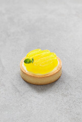 Round tartlet with custard lemon cream and curly lemon jelly on top. Light grey background	