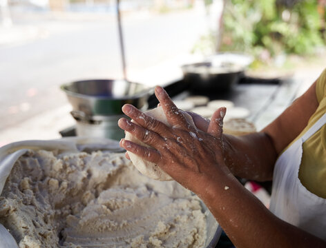 Unrecognizable elderly woman preparing corn tortillas by hand on a griddle in her modest street kitchen